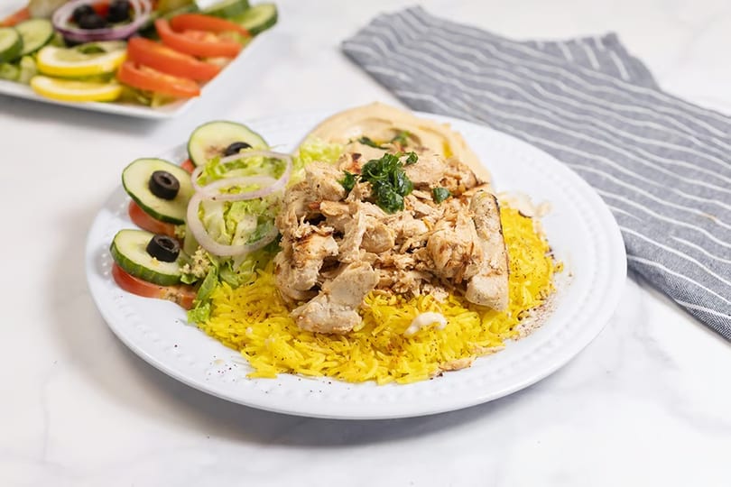 Chicken shawarma plate with yellow rice, hummus, and a side salad with cucumbers and tomatoes.
