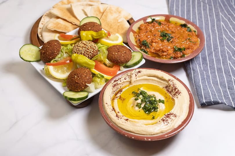 A platter of falafel, salad, pita bread, hummus, and a bowl of ful medames.